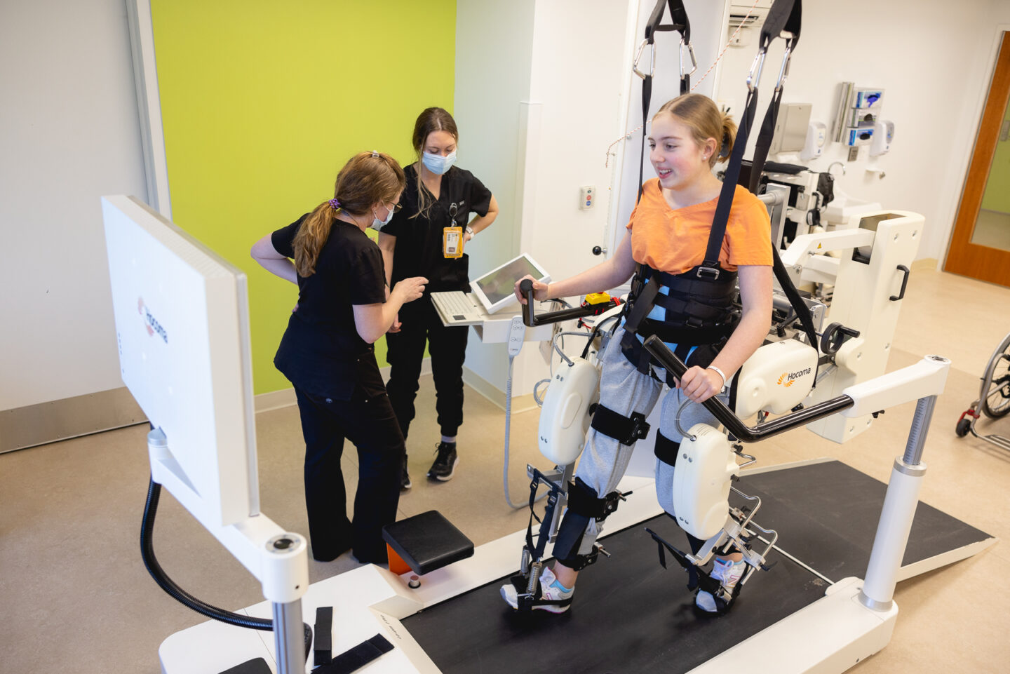A young patient walking in a robotic gait trainer while two therapists assist