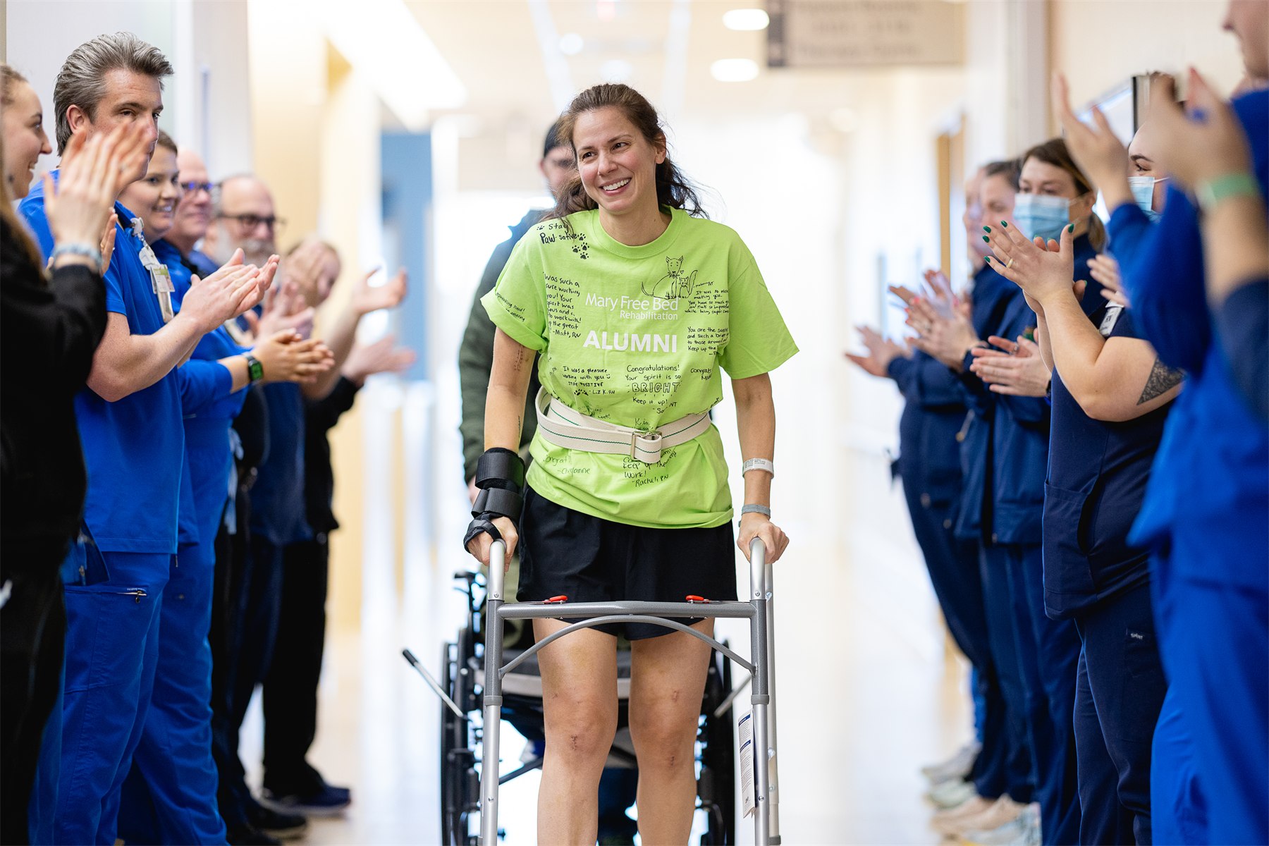 A patient walking with a rolling walker down a hallway lined with applauding Mary Free Bed staff
