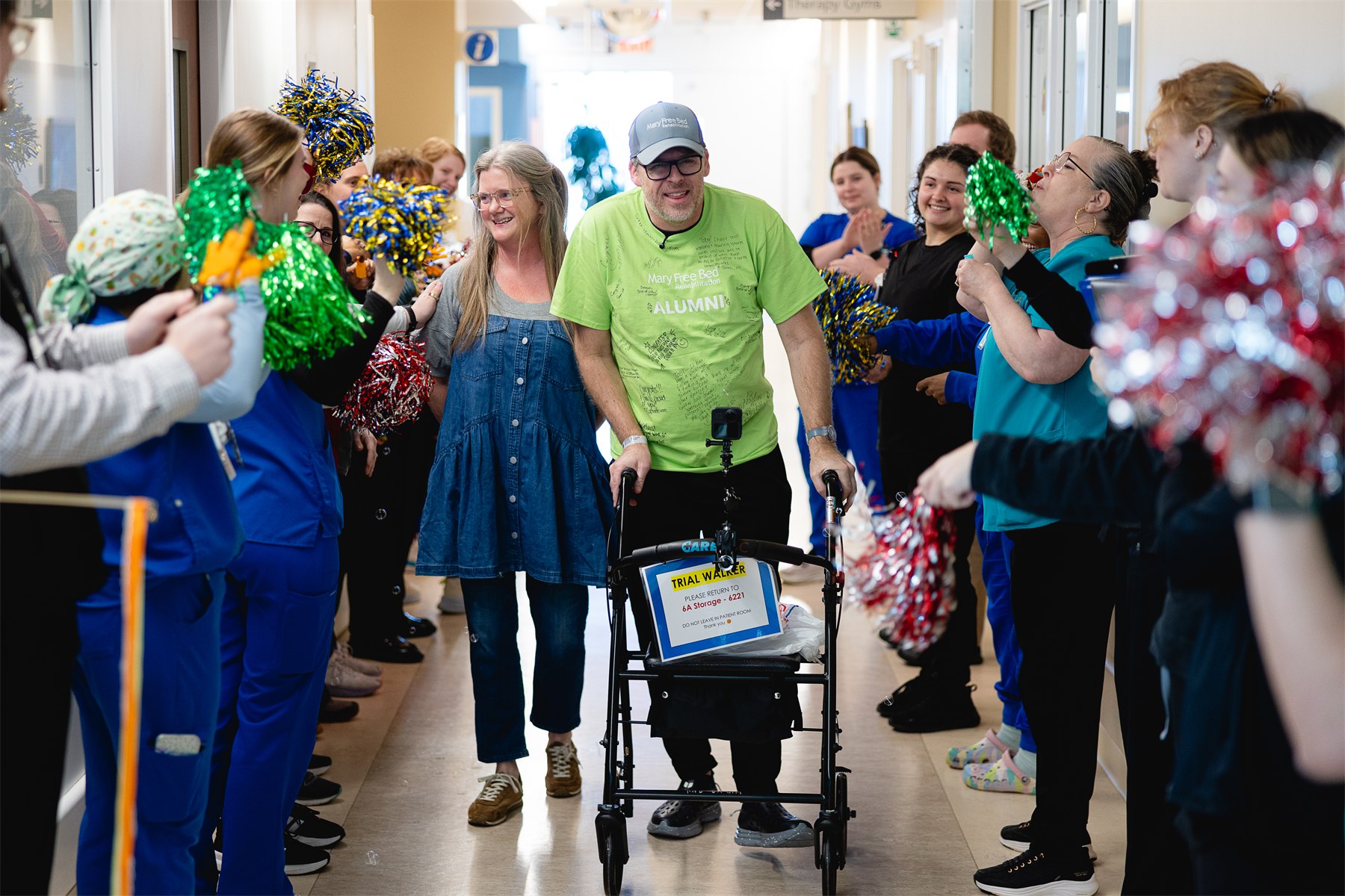 A patient and his mother walking down a hallway of Mary Free Bed staff cheering with pom-poms