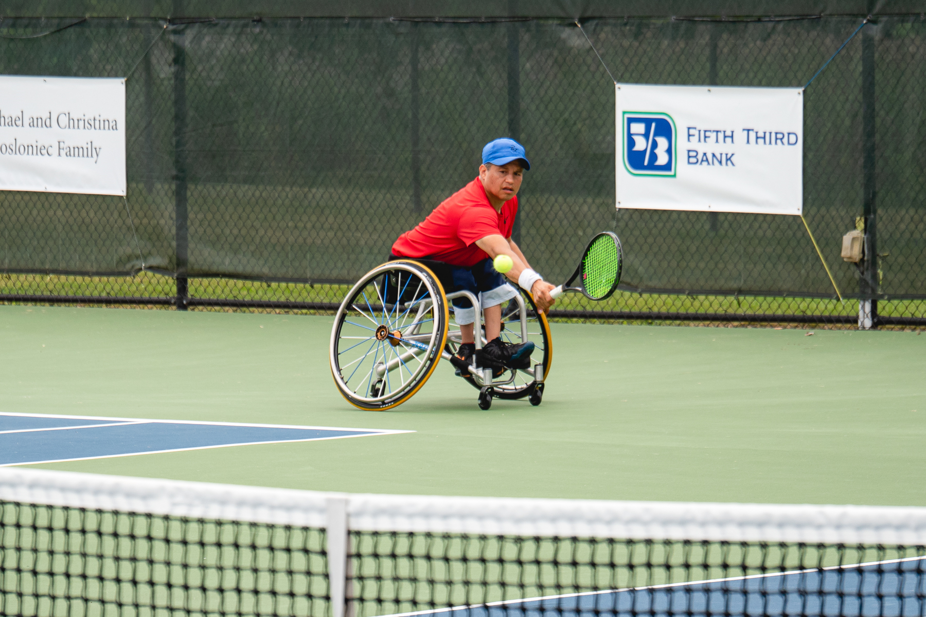 A wheelchair tennis player returning a shot on a court with a Fifth Third Bank banner behind him
