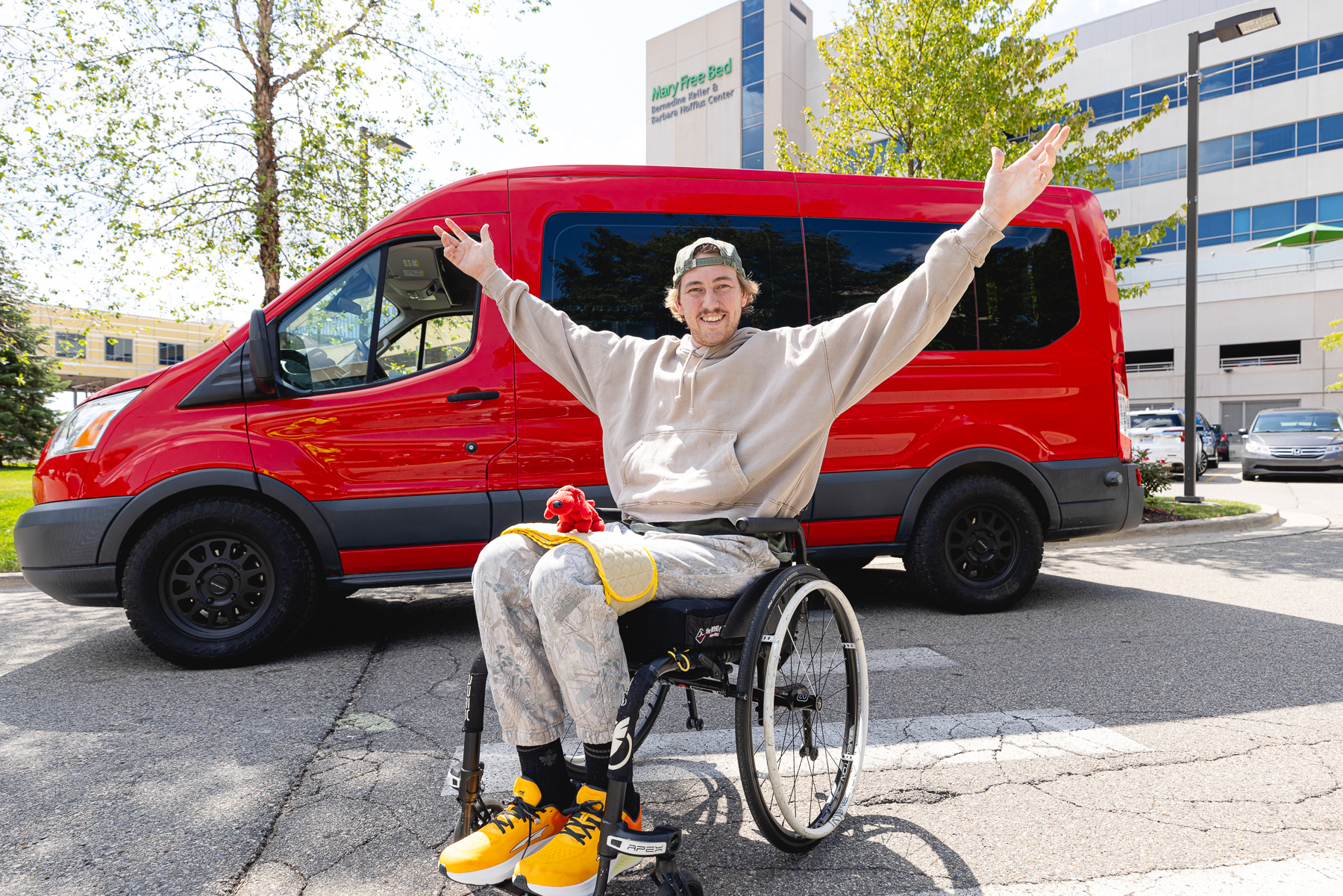 Jason in his wheelchair with his arms raised outside Mary Free Bed