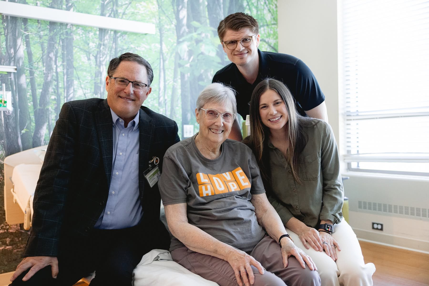 An older patient seated with three family members in her hospital room