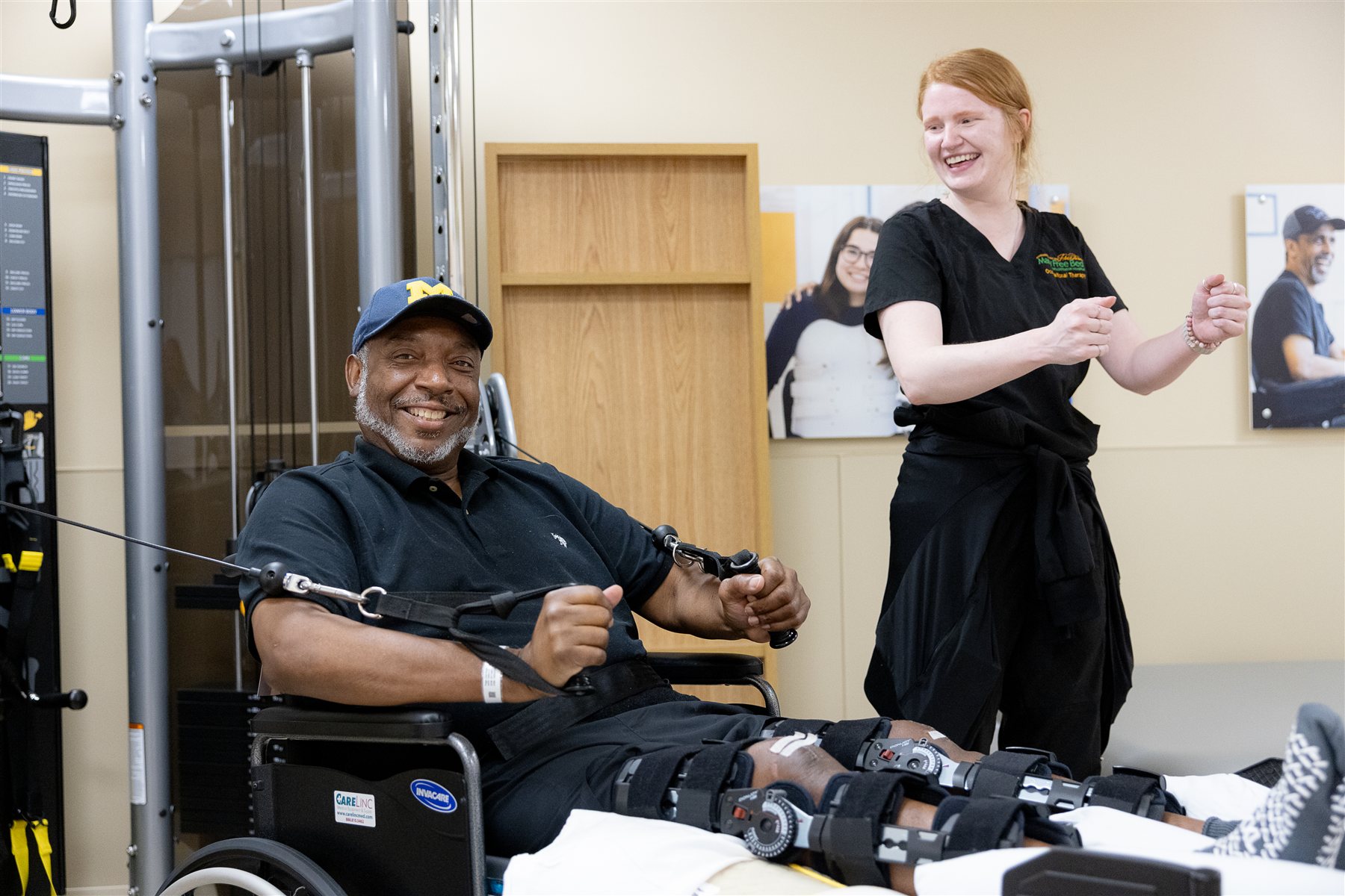 A smiling patient in a wheelchair works with resistance cables while his physical therapist cheers him on