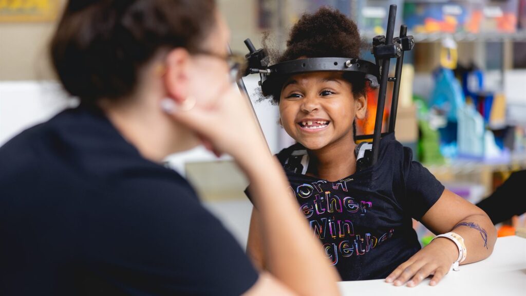 A smiling young patient wearing a halo brace during a therapy session