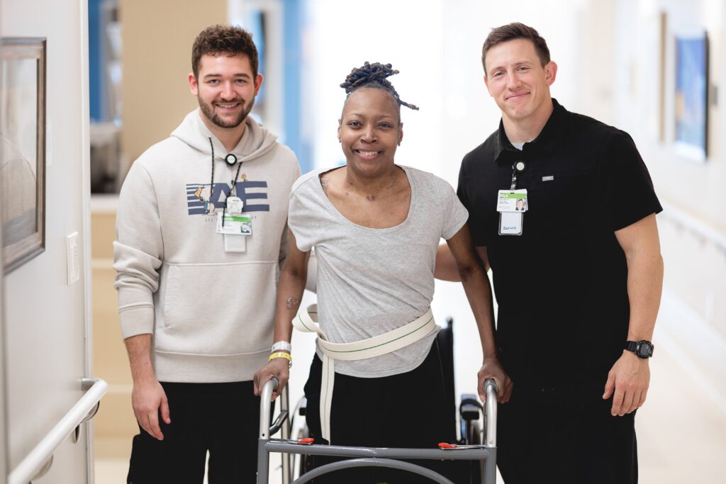 A patient using a walker stands smiling between two members of her care team