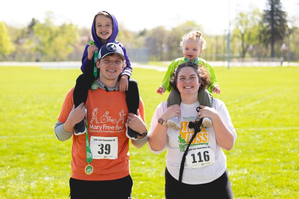 A smiling family carries two young children on their shoulders at a Mary Free Bed race
