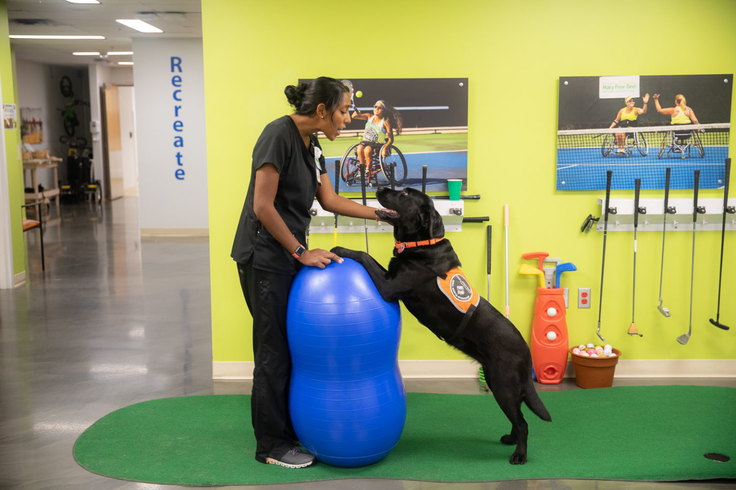 Katie Harrington, Mary Free Bed recreational therapist, works with Vandy, a black Labrador Retriever, using a balance ball in an animal-assisted therapy session.