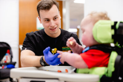 Mary Free Bed therapist in blue gloves helping a young child in adaptive seating practice fine motor skills during pediatric therapy