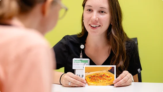 Pediatric speech-language pathologist showing a food photo card to a young patient during a feeding therapy session