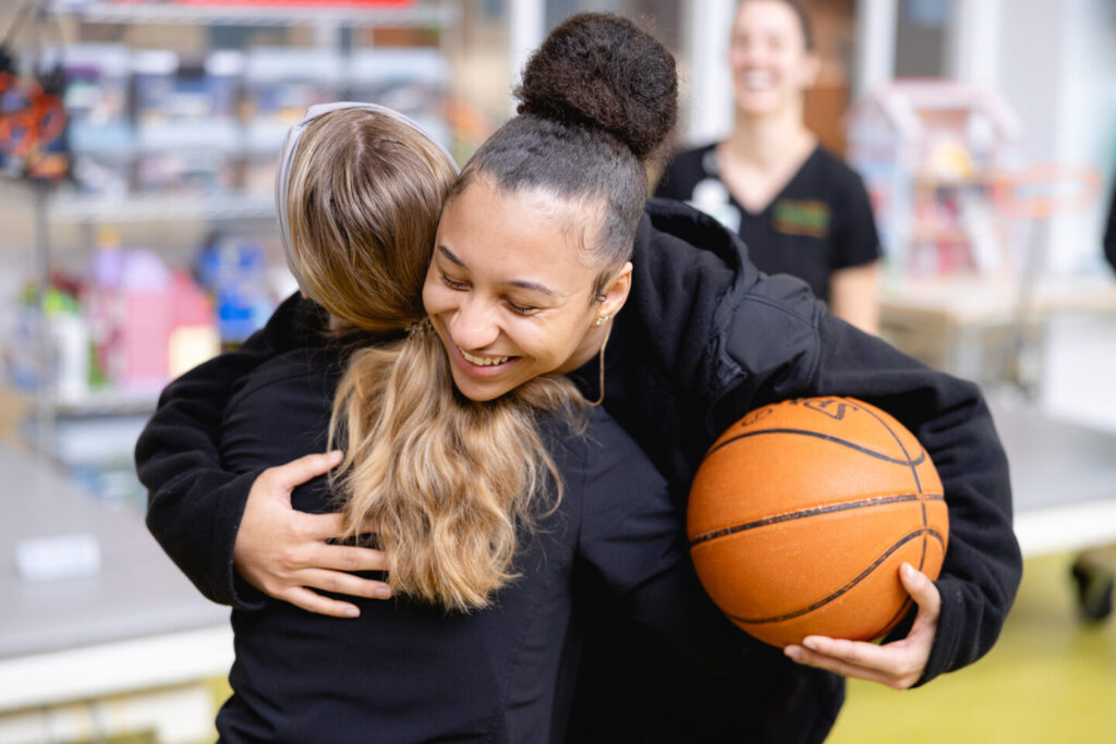 Smiling teen girl holding a basketball hugs a person during a pediatric rehabilitation session at Mary Free Bed