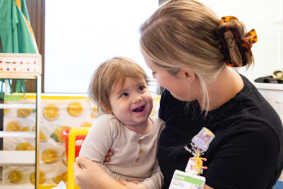 Smiling toddler girl held by a Mary Free Bed pediatric therapist during a therapy session in a colorful treatment room