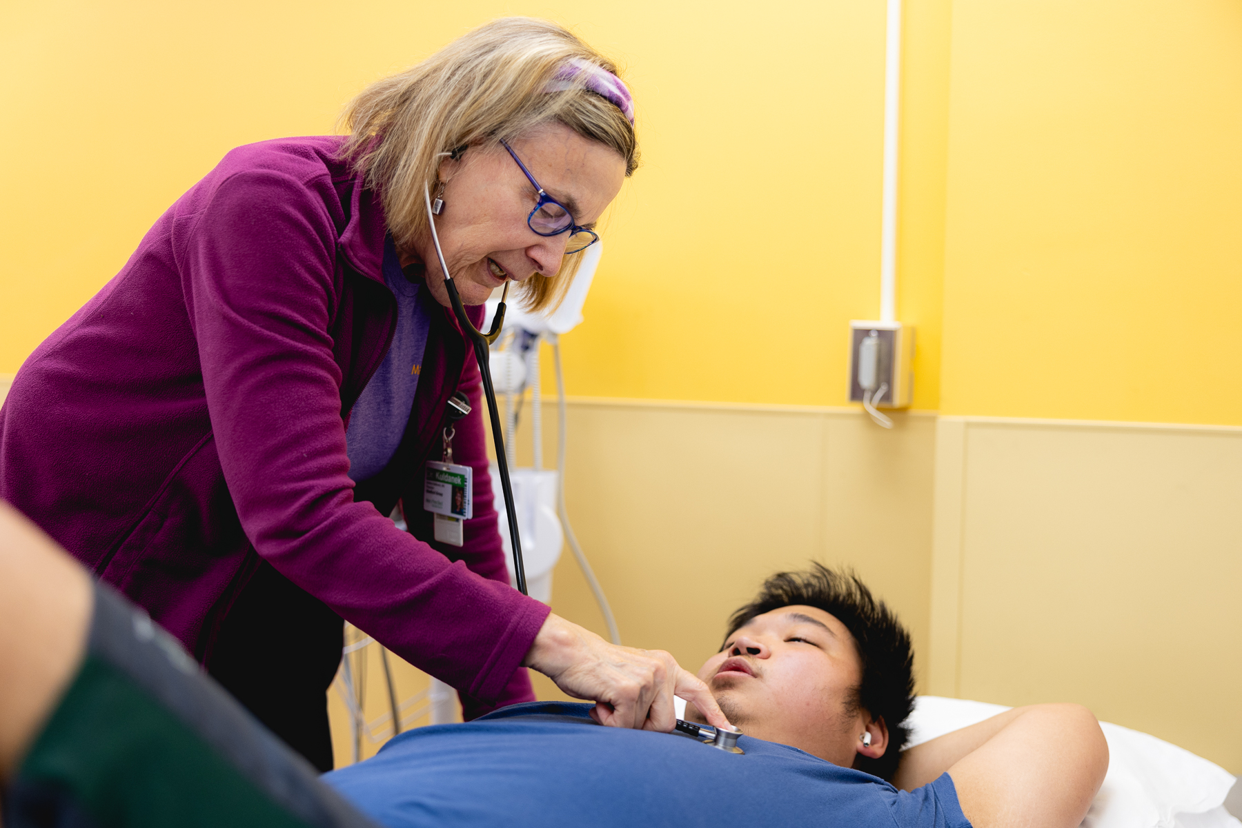 A Mary Free Bed pediatric physician uses a stethoscope to examine a young male patient lying in a hospital bed