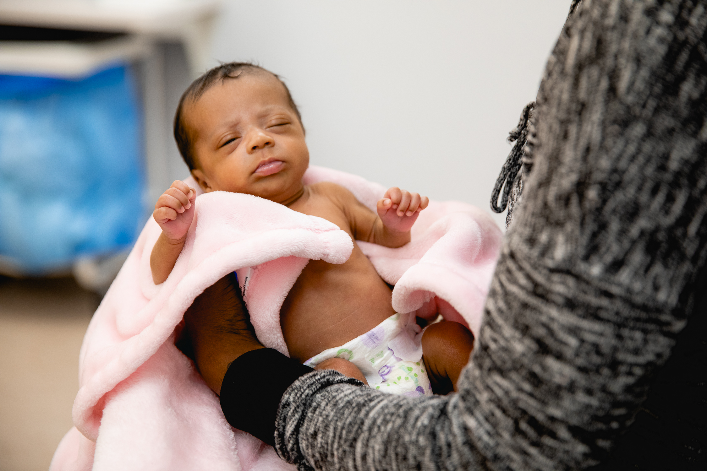 Newborn baby wrapped in a soft pink blanket, cradled in a caregiver's arms during a pediatric care visit