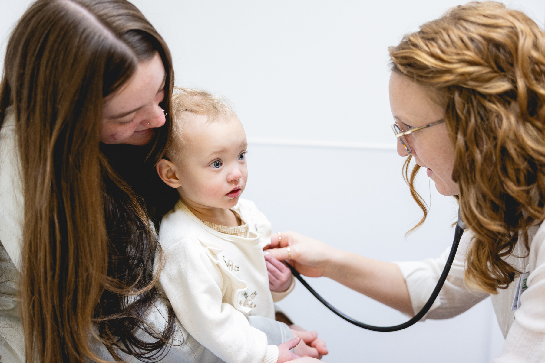 A Mary Free Bed pediatric clinician uses a stethoscope to examine a toddler held by their parent during a medical appointment