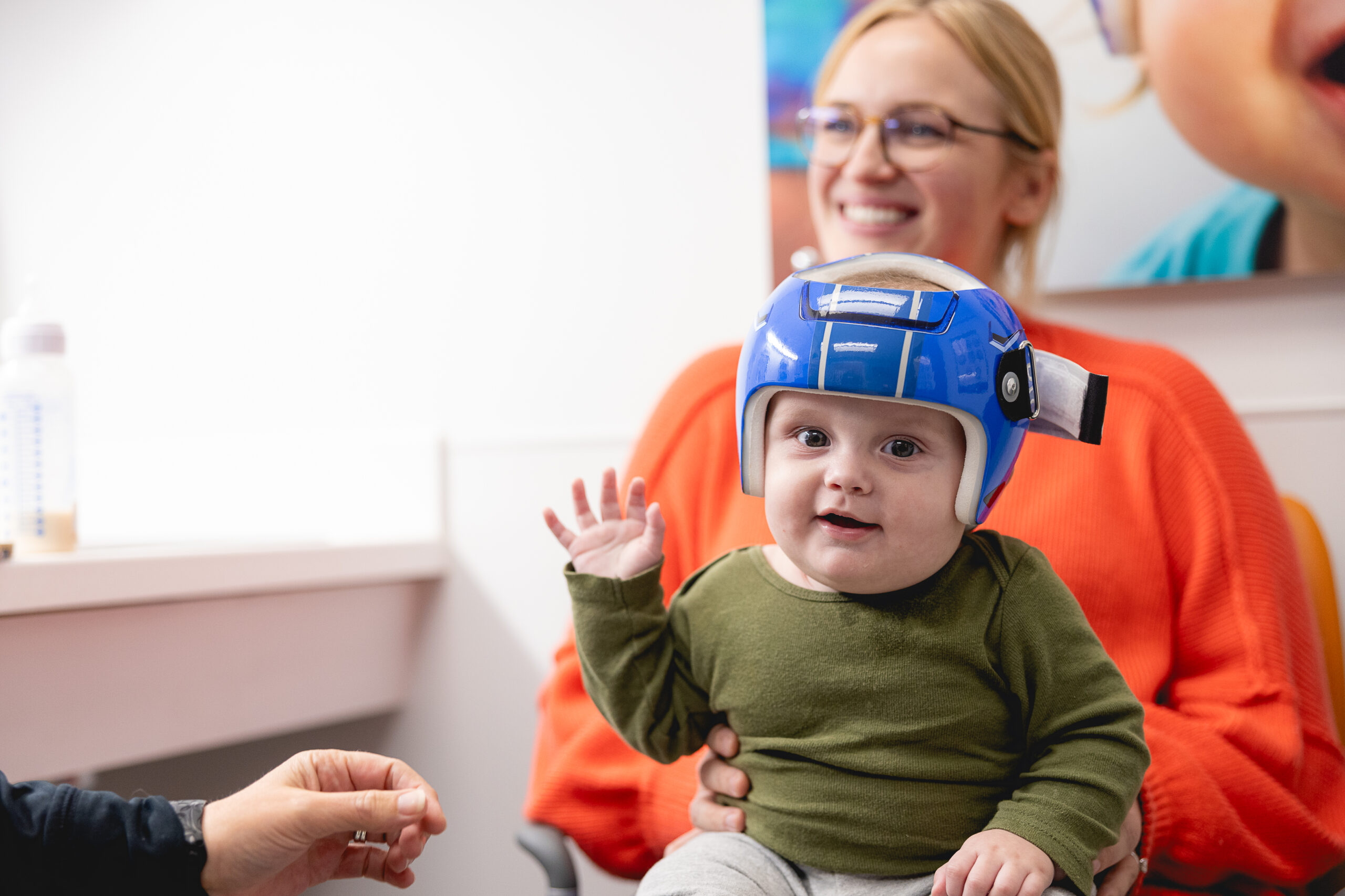 A child in a cranial remolding helmet waving to the camera.