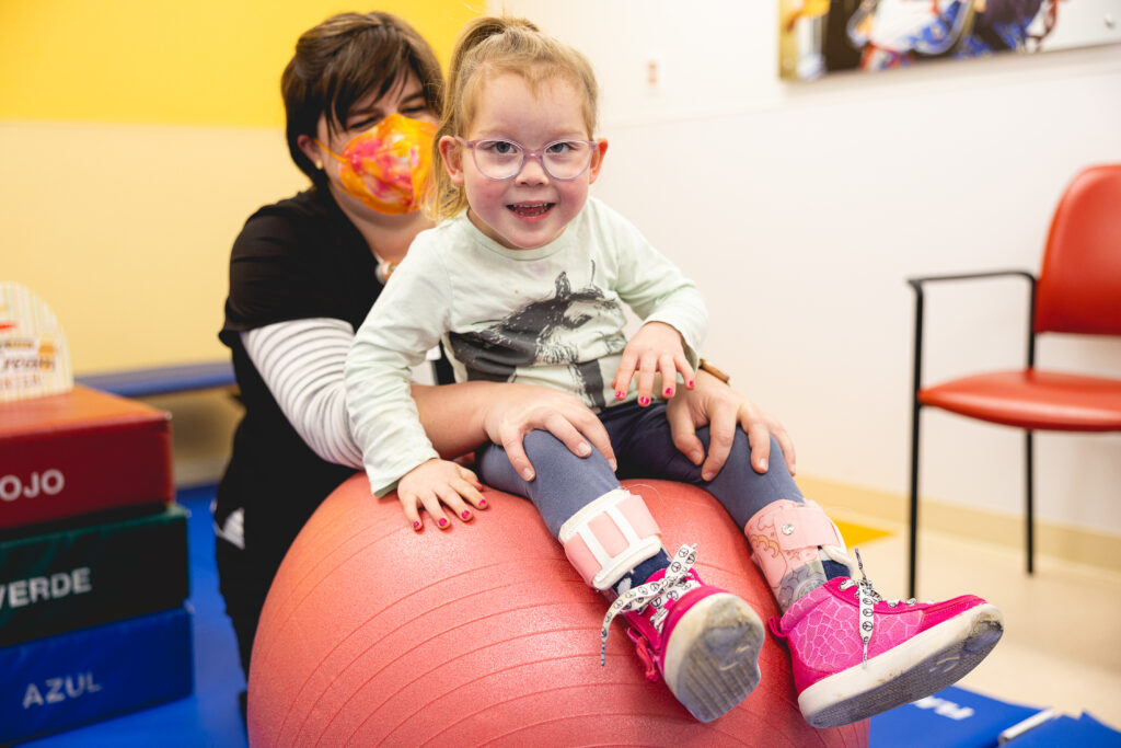 a pediatric patient sits on an exercise ball while a therapist supports them