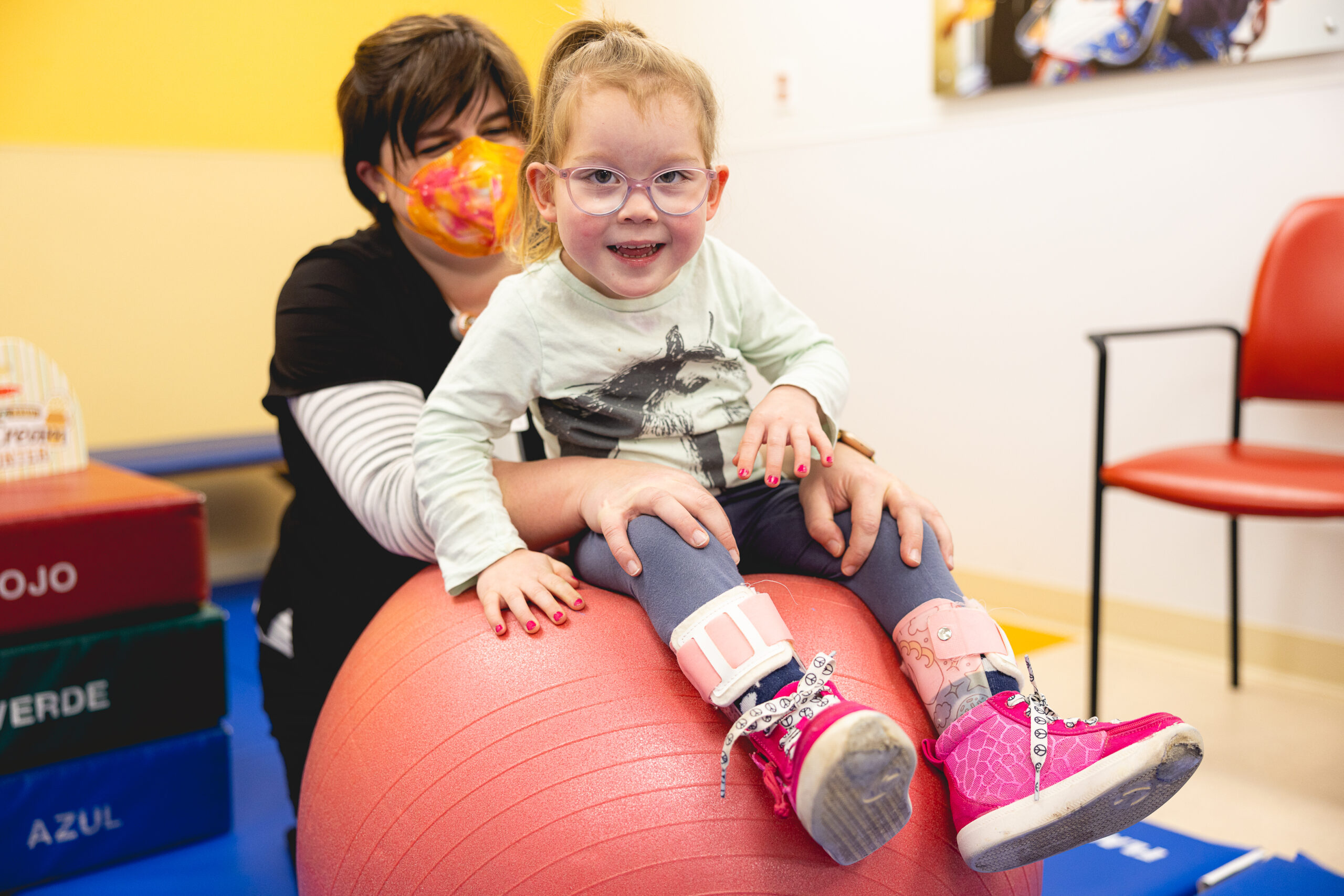 a pediatric patient sits on an exercise ball while a therapist supports them