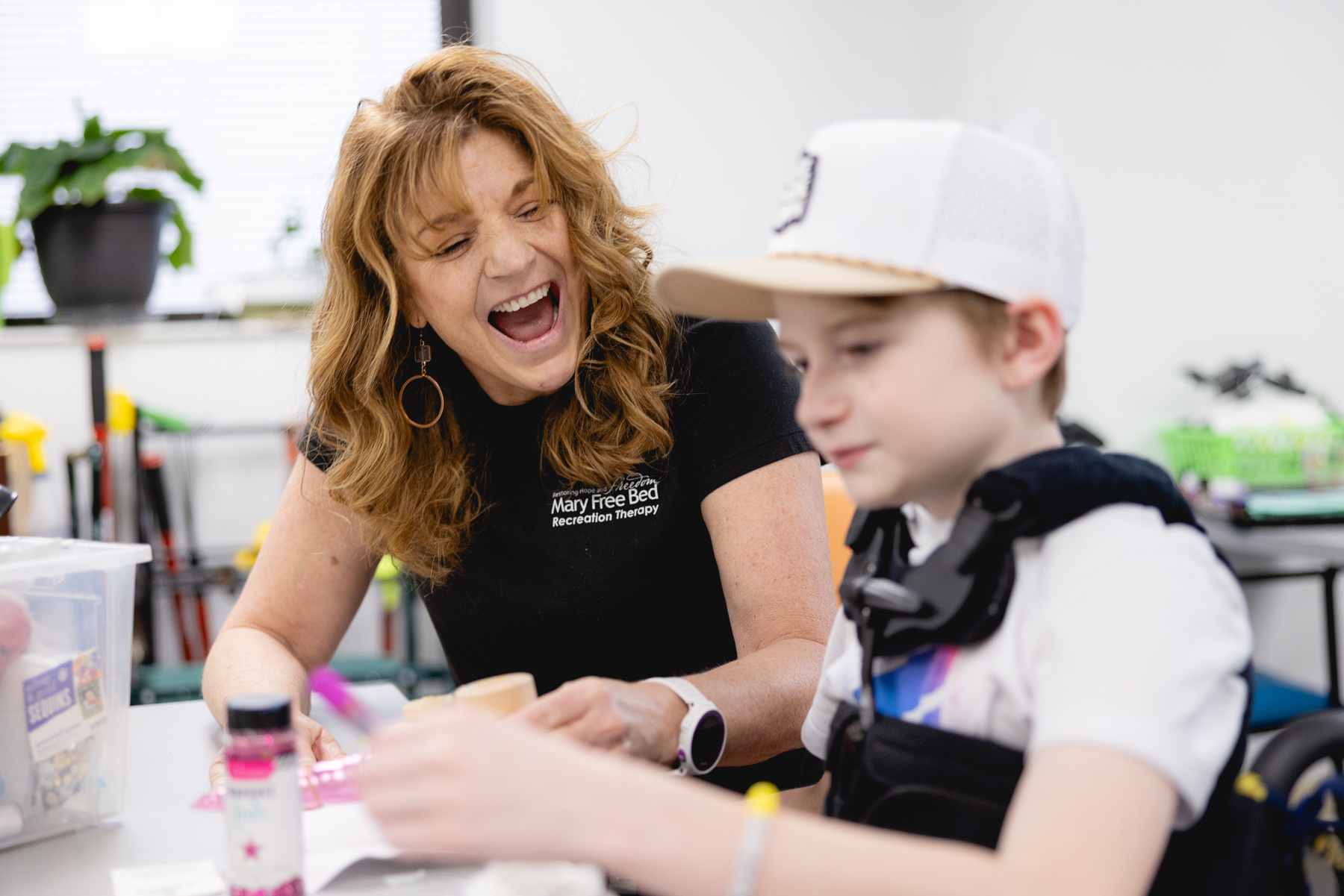 Mary Free Bed recreation therapist laughing with a young child in a supportive vest during a pediatric therapy activity session