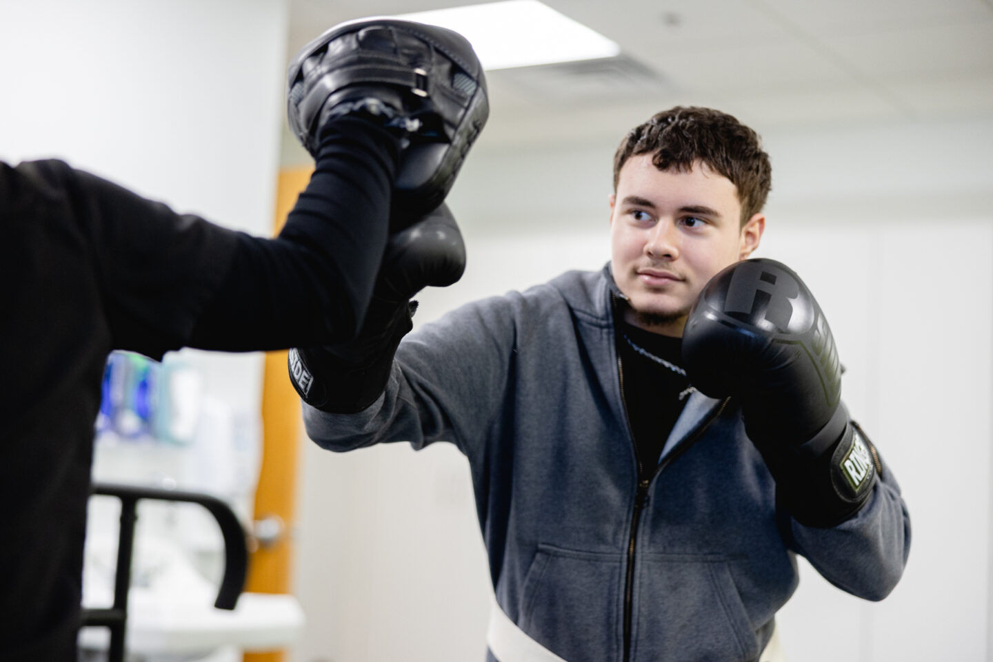 Teen patient wearing black boxing gloves practices punching drills with a therapist during a Mary Free Bed pediatric rehabilitation session