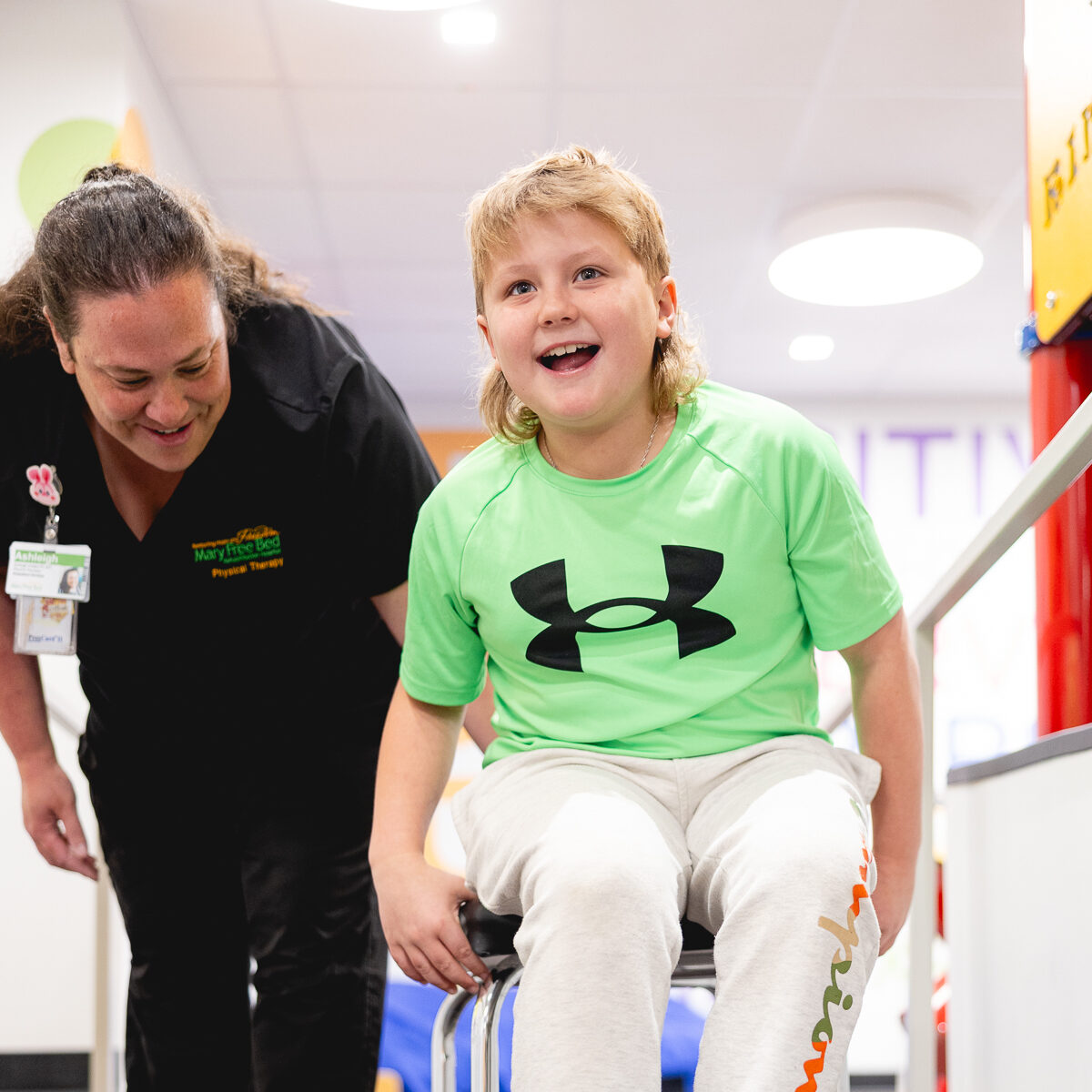 Smiling child using a pediatric walker during physical therapy session with a Mary Free Bed therapist in a rehab facility