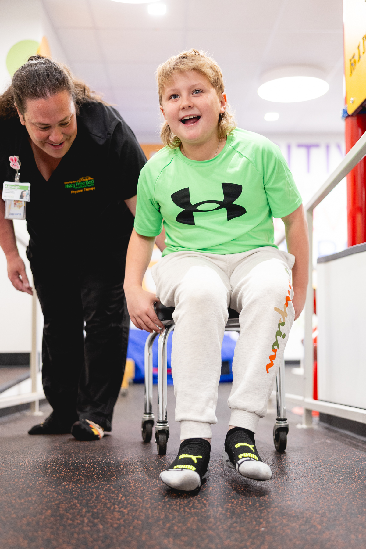 Smiling child using a pediatric walker during physical therapy session with a Mary Free Bed therapist in a rehab facility