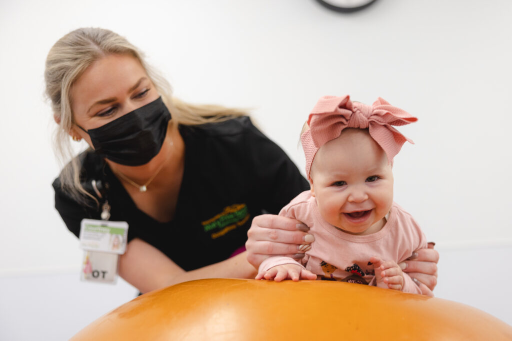 An occupational therapist holding a infant patient on a exercise ball.