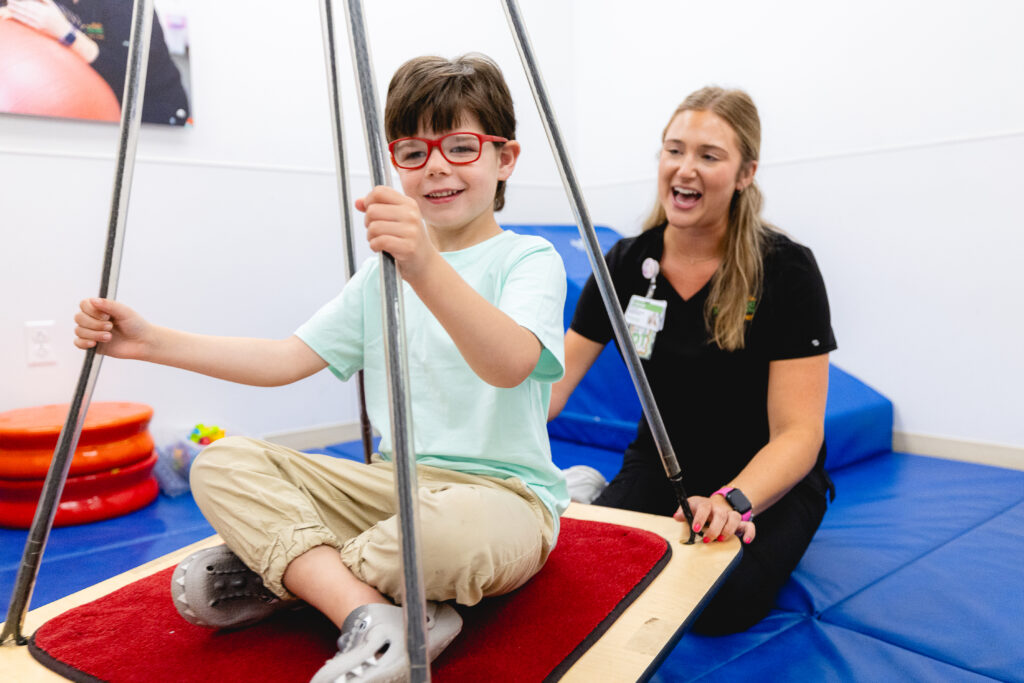An occupational therapist pushing a pediatric patient on a therapy swing
