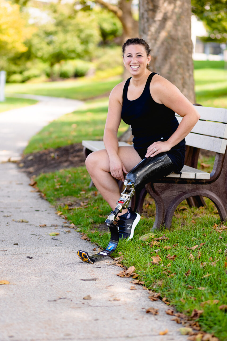 Woman in running attire sits on park bench and smiles at camera.