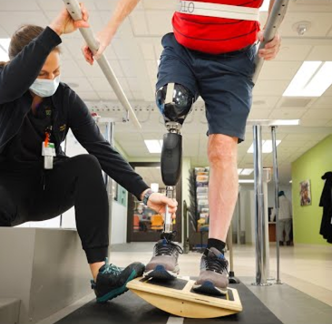 Physical therapist assisting a patient with a prosthetic leg begin to walk