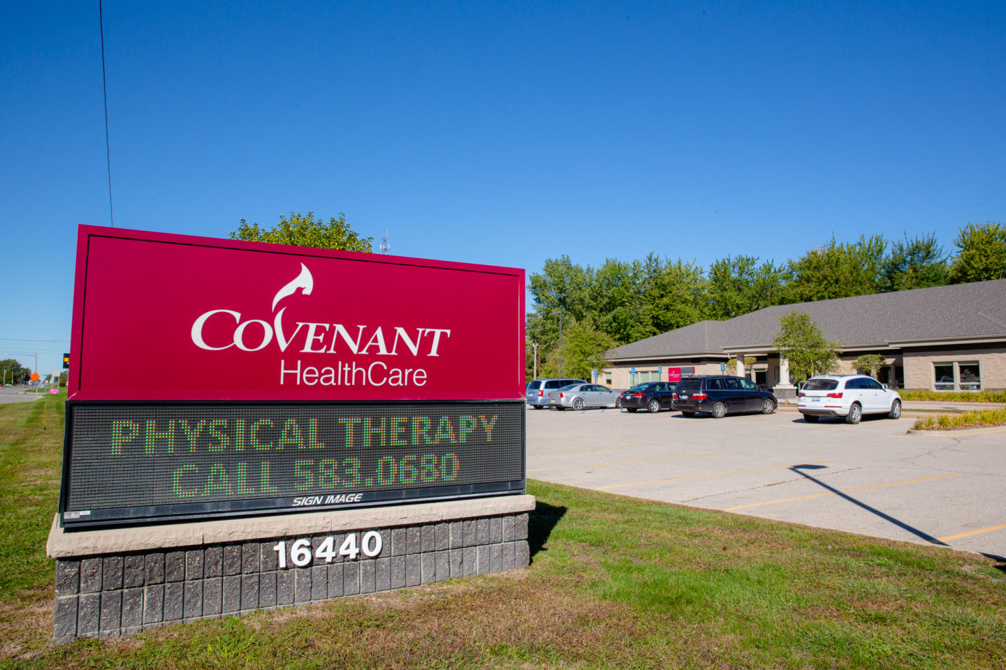 Covenant HealthCare sign displaying physical therapy services and contact number, with a parking lot and clinic building in the background under a clear blue sky.