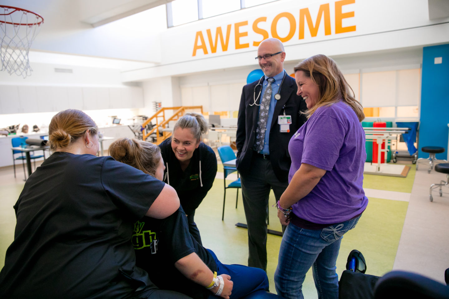 Physical Therapist Cara Hudson, left, and PT assistant Starr Sutton, center, work with Savanah DeHart in the Mary Free Bed Kids therapy gym. Dr. Douglas Henry and Savanah's mother, Kerri Dooley, watch her progress.