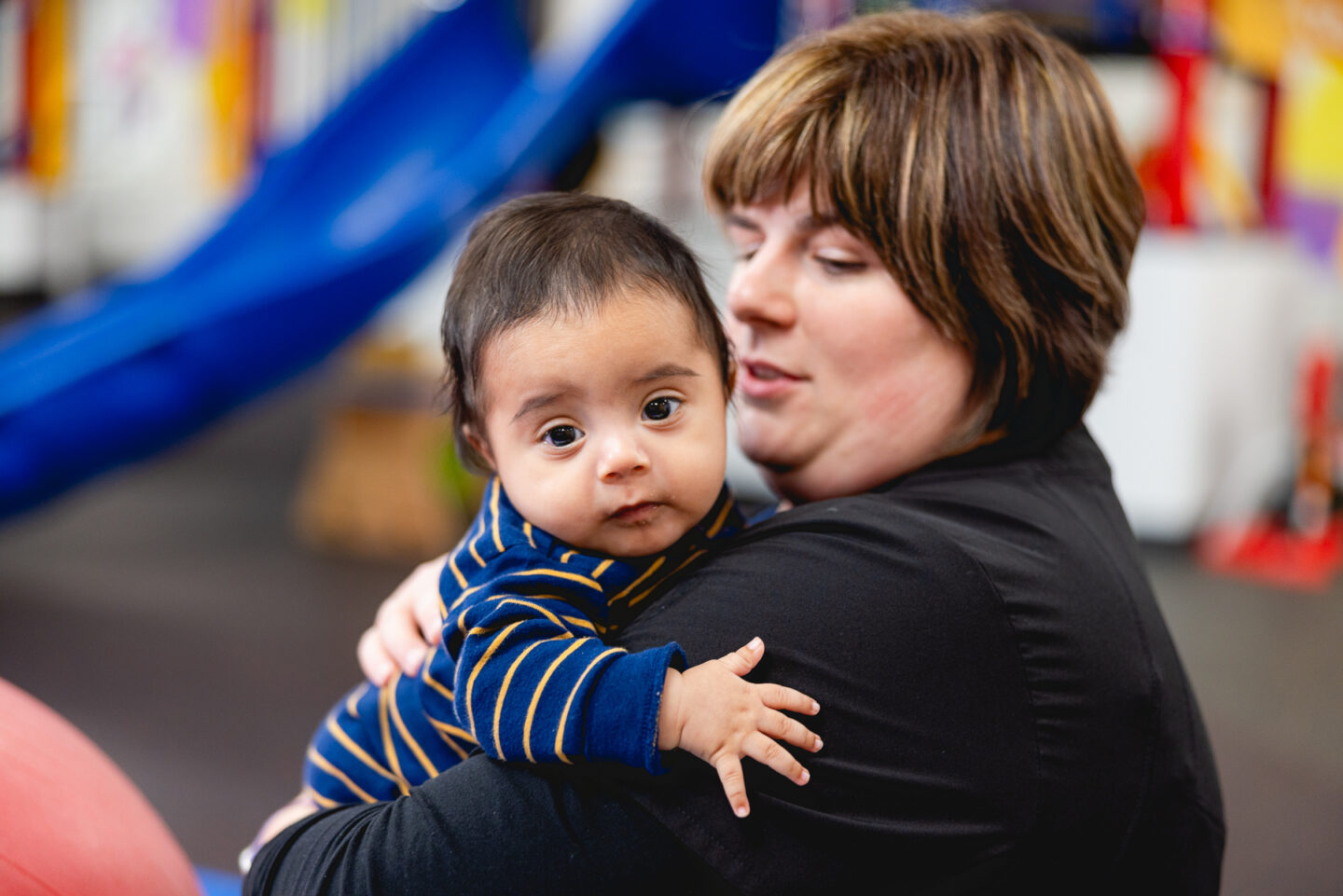 Infant hugging physical therapist and smiling at the camera