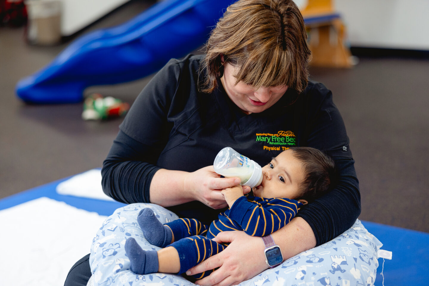 infant drinks bottle while being held up by physical therapist