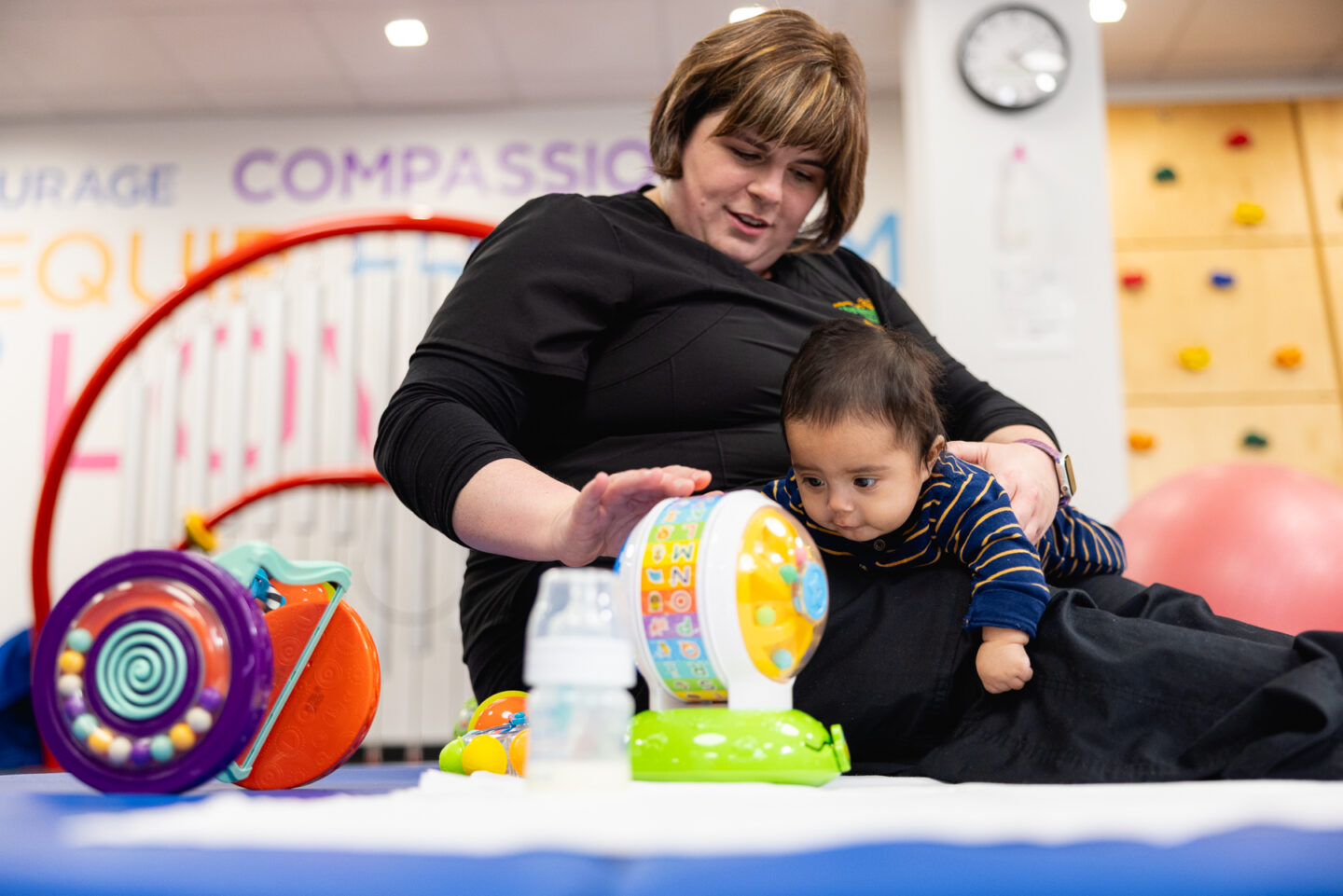 infant plays while laying across the physical therapist