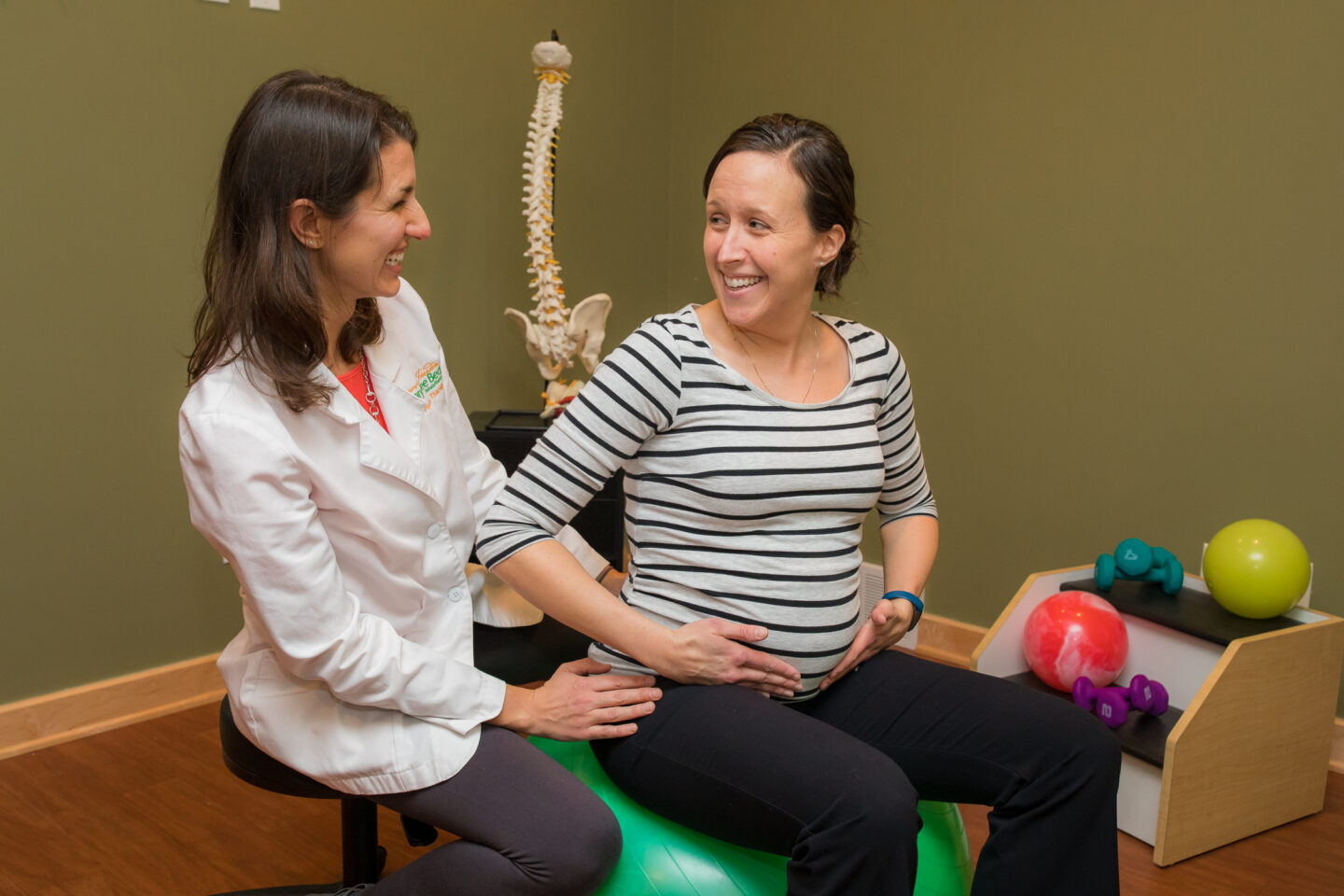 A physical therapist assists a patient with pelvic exercises on a stability ball.