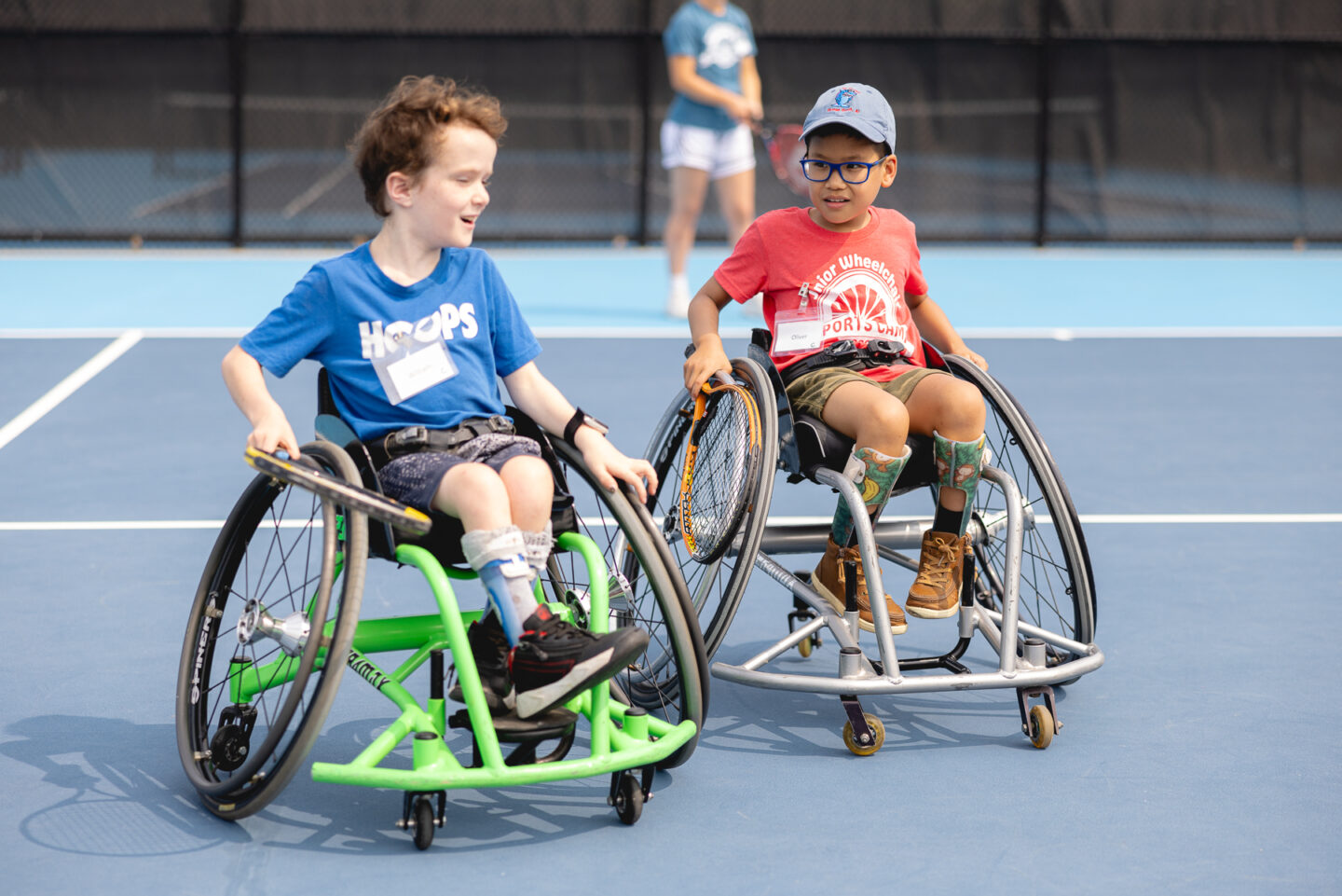 Two kids in wheelchairs playing tennis on a blue court.