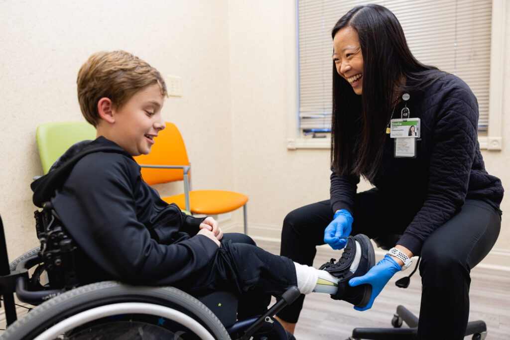 A young patient in a wheelchair laughs during his orthotics fitting.