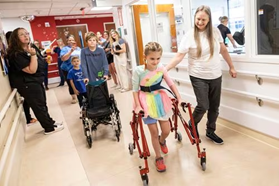 In The Media 57 Young patient, Bella, using a walker, being helped along by professionals.