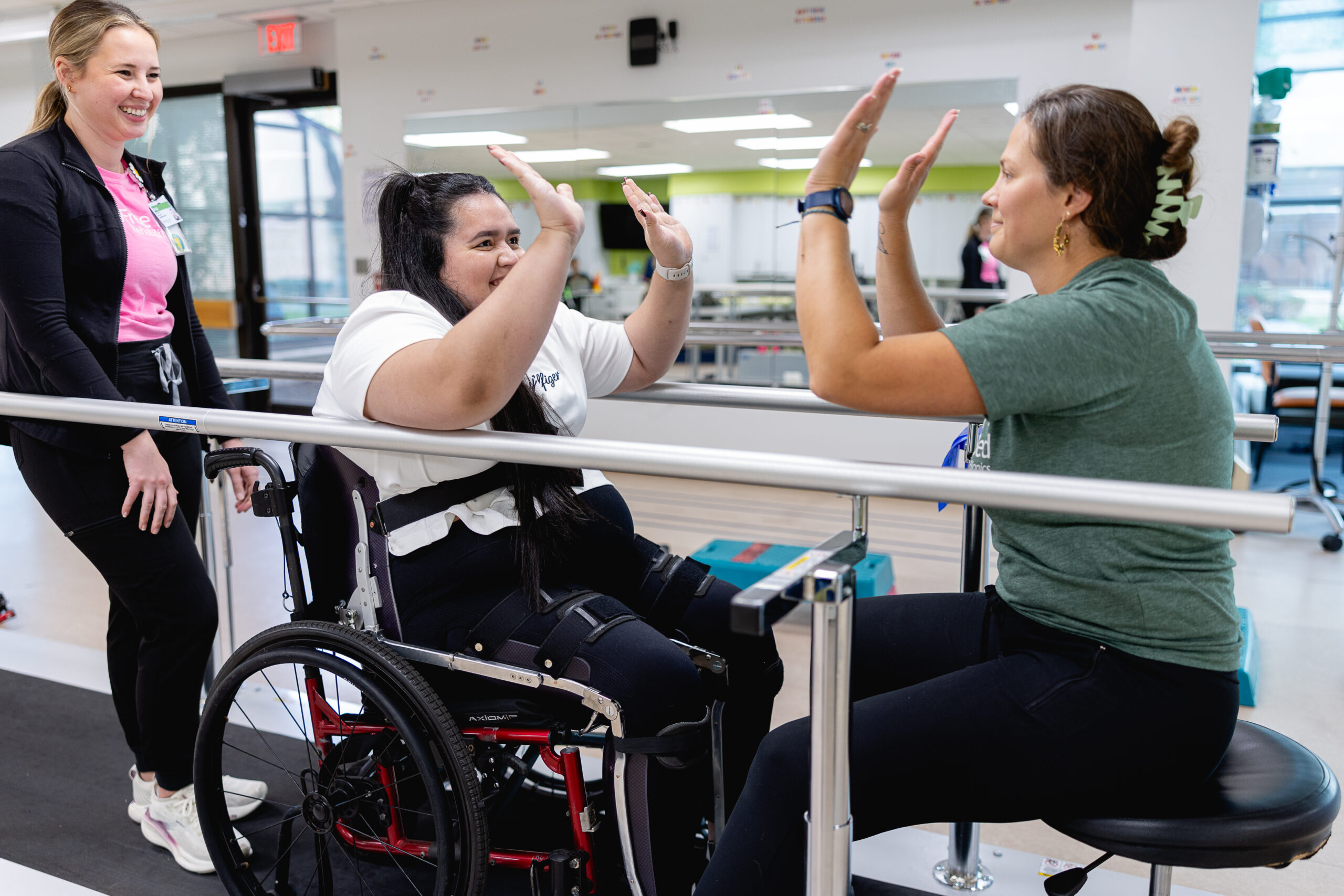 A patient in a wheelchair high-fiving a therapist while another watches.