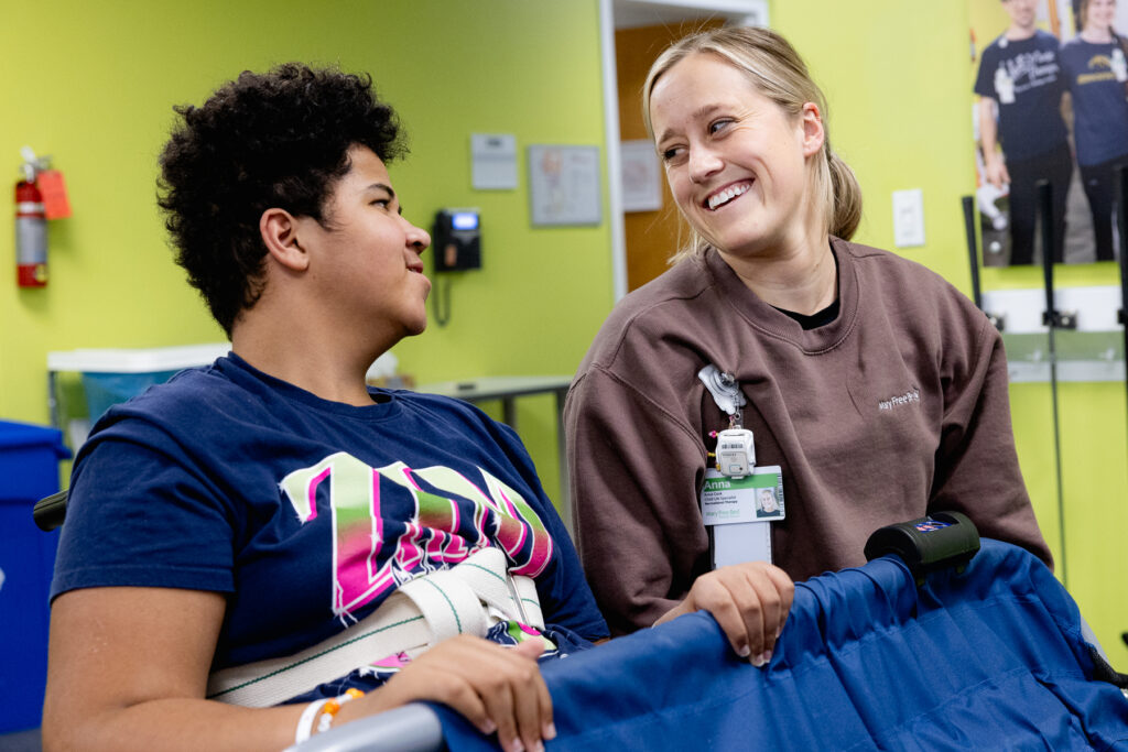 Child life specialist engaging with a young patient in a bright therapy room, sharing a supportive moment during pediatric rehabilitation and emotional support care