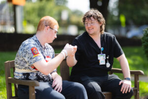 Pediatric physical therapist working with a young child outdoors on a wooden bench, performing hand exercises and movement activities to support motor skill development and rehabilitation
